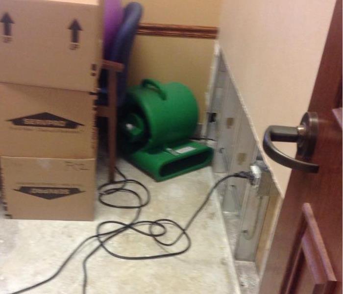 Removed flooring and dry wall with green drying equipment up and running next to cardboard SERVPRO boxes.