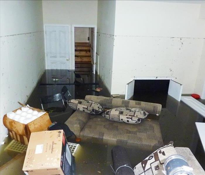 Basement with flooded waters, there is a couch, chairs, and boxes floating aorund